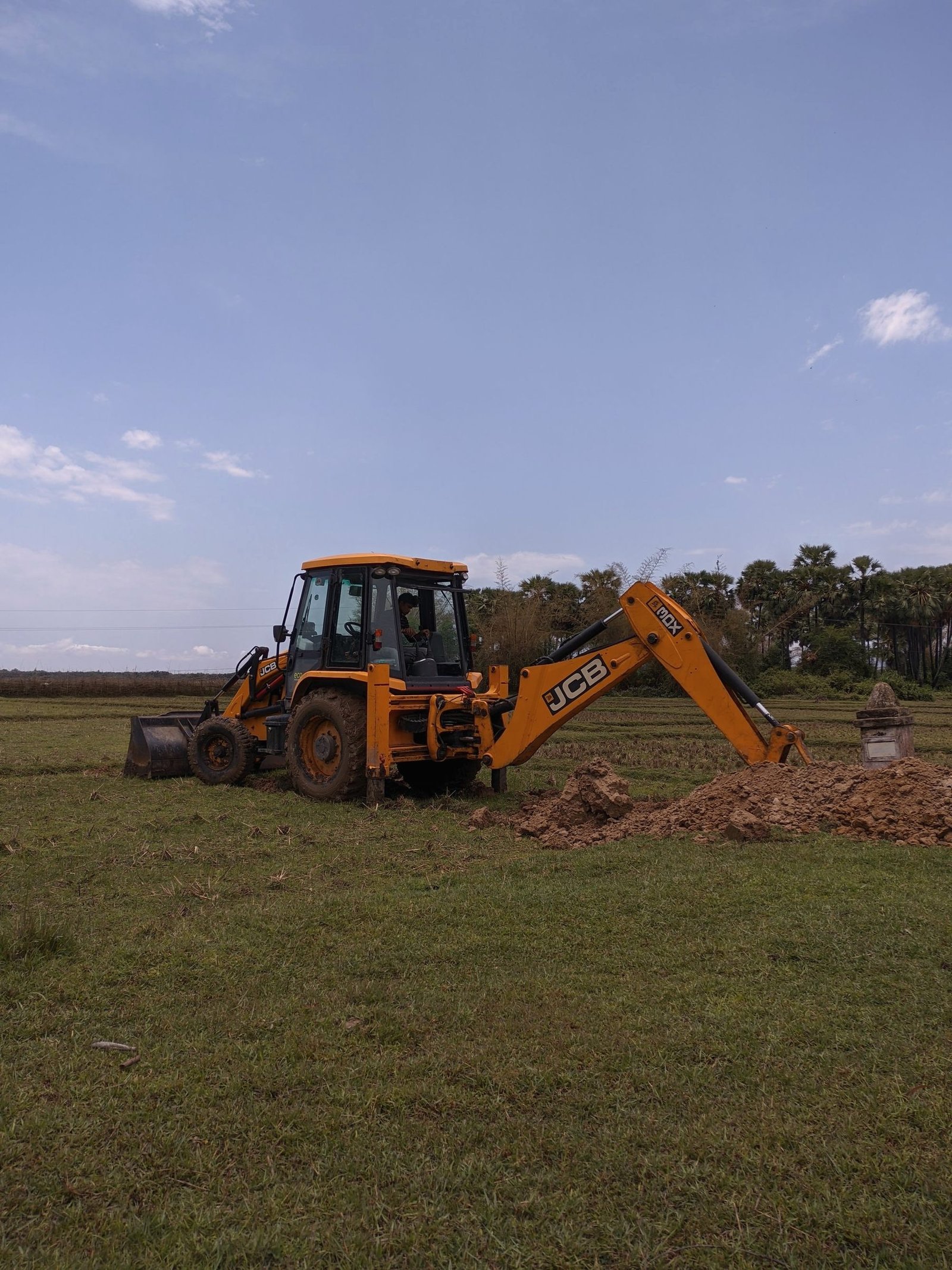A backhoe loader working open ground at the edge of a field